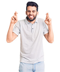 Wall Mural - Young handsome man with beard wearing casual polo gesturing finger crossed smiling with hope and eyes closed. luck and superstitious concept.