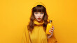 © Surachetsh - A young woman is showing yellow orange liquid bottle like a honey, oil, or orange juice. She is Standing in front of vivid yellow background with the same her yellow cloth color. Generative AI.