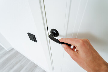 Hand gesturing to open a white door with a black handle