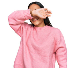 Wall Mural - Young asian woman wearing casual winter sweater covering eyes with arm smiling cheerful and funny. blind concept.