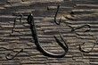 Steel fishing hooks of various sizes on a background of rough wood texture. Selective focus.