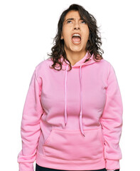 Wall Mural - Young hispanic woman wearing casual sweatshirt angry and mad screaming frustrated and furious, shouting with anger. rage and aggressive concept.