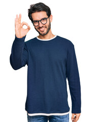 Wall Mural - Young hispanic man wearing casual clothes and glasses smiling positive doing ok sign with hand and fingers. successful expression.