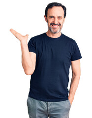 Wall Mural - Middle age handsome man wearing casual t-shirt smiling cheerful presenting and pointing with palm of hand looking at the camera.