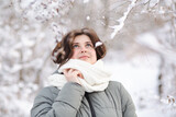 Fototapeta Koty - young woman looking up on winter nature, pretty beautiful girl among trees covered with snow walking in white forest and enjoying