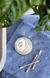 Fototapeta Boho - Opened cream jar on blue towels near basin and green monstera in bath, beauty routine