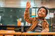 portrait cute black boy of 7 years old,sitting in modern classroom among and taking an active part in learning,raising his hand,concept of educational materials,development and upbringing of children