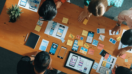 Top view of software developer team looking Ux Ui design for mobile phone interface from tablet while comparing and planning wireframe prototype designing together at creative workplace. Convocation.