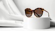Woman's Tortoiseshell frame sunglasses on a podium on a white background. Trendy sunglasses still life, minimal style. Summer fashionable accessories. Optic store discount, sale, promotion. Copy space