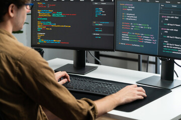 IT developer working online software development on pc monitors at modern home office on coding application screens, creating updated latest program firmware information version concept. Gusher.