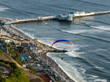 A paraglider flies over the traffic on the Costa Verde in Miraflores, Lima, Peru. You can see the avenue full of cars, the sea and a building on a breakwater.