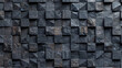 A black and gray stone wall with a rough texture. The wall is made up of many small square blocks