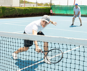 Wall Mural - Young man in shorts and t-shirt playing tennis on court. Racket sport training outdoors