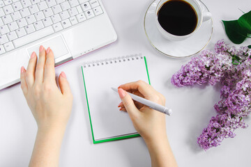 Woman works at home on laptop in morning. Cup of coffee and lilac flowers on table.