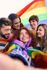 Vertical. Fun selfie LGBT group young friends celebrating gay pride day together holding rainbow flag. People community smiling and taking cheerful portrait outdoor. Generation z positive relations.