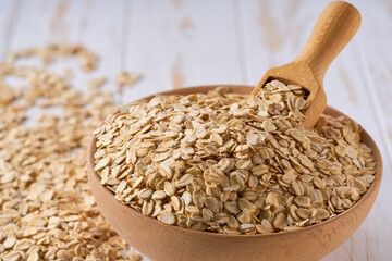 Raw oatmeal flakes are scattered in a wooden bowl close up.