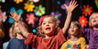 © MNStudio - Kindergarten kids participating in spring themed school play. Cheerful children performing on theater stage in front of their parents. Creative leisure for elementary school students.