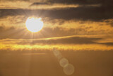 Fototapeta  - Zachodzące słońce na mocno zachmurzonym niebie. Słońce kolorowo zachodzące wśród chmur w ostatni dzień kalendarzowej zimy.