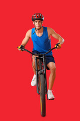 Wall Mural - Young man riding bicycle on red background