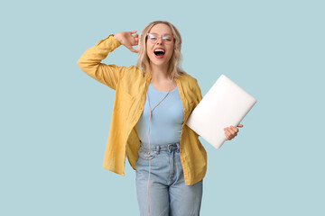 Wall Mural - Pretty young woman with modern laptop and headphones listening to music on blue background