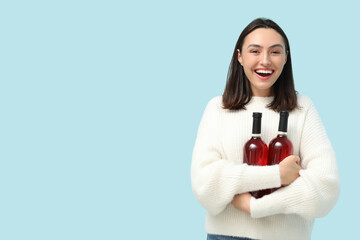 Poster - Beautiful young woman with bottles of red wine on blue background