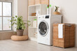 Modern washing machine with basket, shelving unit and dressing screen near white wall. Interior of home laundry room