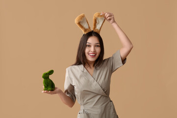 Poster - Female Asian massage therapist in bunny ears with Easter rabbit on brown background