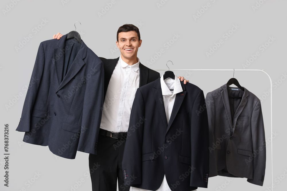 Handsome young happy man and rack with formal clothes on grey background