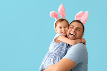 Wall Mural - Happy young man with little daughter in Easter bunny ears on blue background