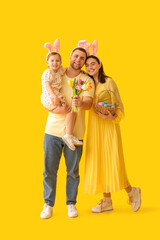 Wall Mural - Happy family in bunny ears holding tulips and basket with Easter eggs on yellow background