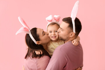 Wall Mural - Happy parents in Easter bunny ears kissing daughter on cheeks against pink background