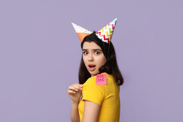 Wall Mural - Beautiful young shocked woman with paper sticker attached to her back on purple background. April fool's day celebration