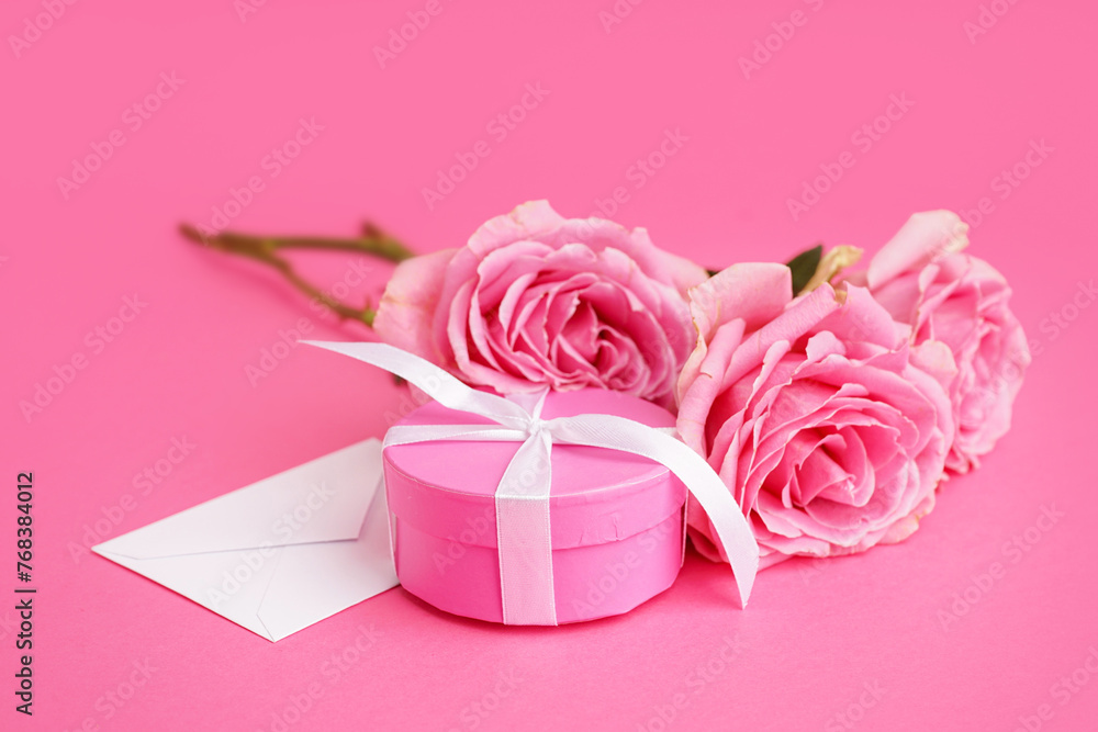 Gift box with envelope and beautiful roses on pink background