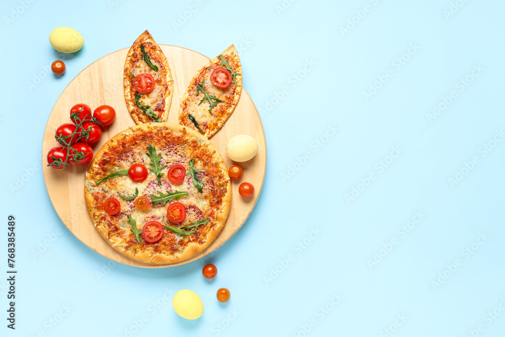 Easter pizza with bunny ears, eggs and tomatoes on blue background