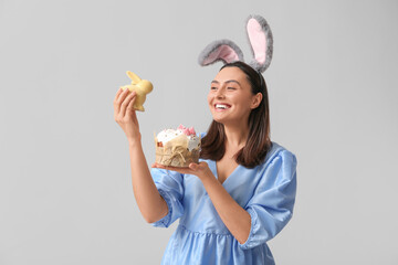 Canvas Print - Beautiful young woman in bunny ears with sweet Easter cake and toy rabbit on grey background