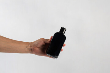 Wall Mural - Black cosmetic bottle in hand isolated on white background.