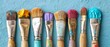   A line of paintbrushes aligned with a blue background, featuring paint splatters on the bristles