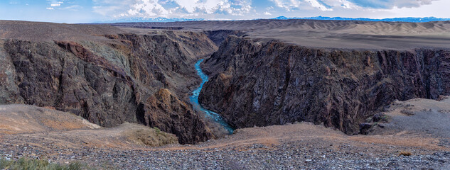 Great Black Charyn Canyon in Kazakhstan. A large huge panorama of a sandy desert landscape with an azure river in the middle against the backdrop of mountains. Sparse vegetation. Big size panorama