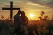 Couple praying God together in field in front of cross at sunset.