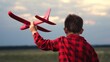 Cheerful male kid running with red airplane toy imagine pilot flight at summer field closeup back view. Adorable playful boy child flying with plane plaything fantasy imagination at evening meadow sky
