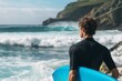 surfer with a blue board underarm looking out at the sea and waves