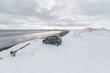 © Cavan Images - Small car parked in front of ocean during winter surf day
