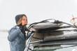 © Cavan Images - Woman removing surf board from roof of car