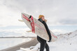 © Cavan Images - Woman walking on beach with surf board winter iceland