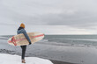 © Cavan Images - Woman standing in front of the ocean with surf board winter iceland
