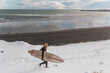 © Cavan Images - Woman walking on beach with surf board winter iceland