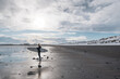 © Cavan Images - Woman walking on beach with surf board winter iceland