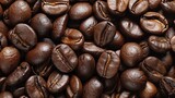 Close-up of roasted coffee beans. Dark brown and oily, the beans are scattered randomly, creating a textured background.
