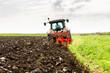 Tractor with plowing equipment preparing the soil in a green field under a clear sky