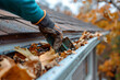 a close-up view, an worker is on the roof of a house. scooping out the eavestrough or roof gutters to clean in preparation for the upcoming winter.